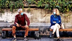 Two older adults sit on benches on a sidewalk