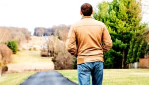 A man walks down a path towards a small cluster of homes