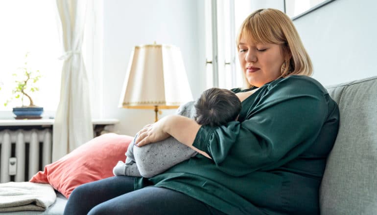 woman nurses new baby on sofa