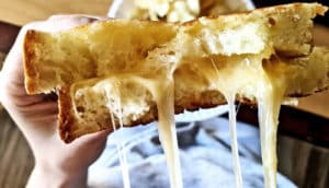 A person holds a broken grilled cheese sandwich with cheese stretching off camera