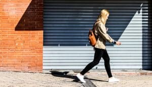 A young woman walks on a sidewalk past a closed metal door in a brick building