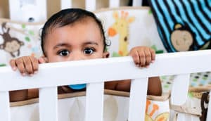 A baby peeks out from a crib while holding onto the side