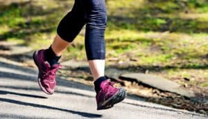 A woman runs on a park path while wearing purple running shoes