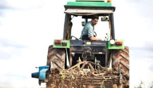 A farmer on a tractor looks backward as machinery harvests potatoes