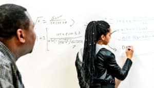 teacher looks on as Black female student does math on white board