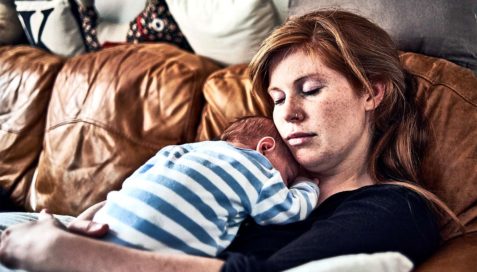 A mother lays on a couch with her baby on her chest.