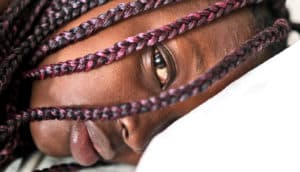 A young woman looks tired as she opens her right eye while her head is on a white pillow