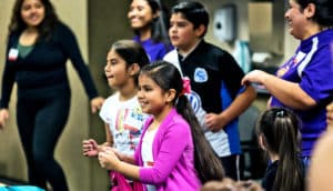 Children and parents move together while watching an instructor.