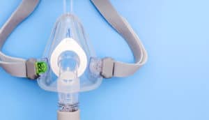 A CPAP mask and head strap sits on a pale blue background.