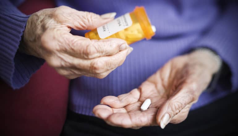 hands of elderly person hold pill bottle and pill
