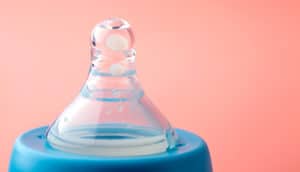 A baby bottle top against a pink background.