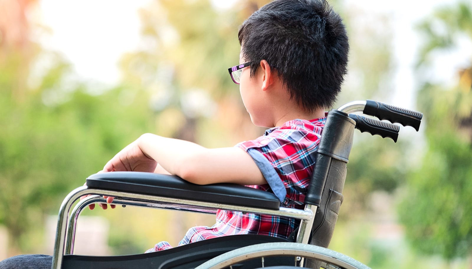 A young boy in a wheelchair looks into the background while outside.