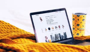 laptop showing instagram page on gold blanket with travel mug