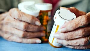 An older woman looks over multiple pill bottles in her hands.