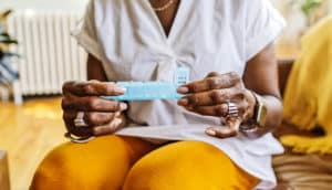 A woman holds a daily medication organizer while sitting in her living room.