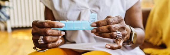 A woman holds a daily medication organizer while sitting in her living room.