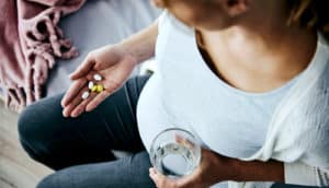A pregnant woman holds pills in one hand and a glass of water in the other.
