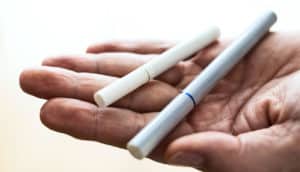 A man holds a cigarette and an e-cigarette in the palm of his hand.