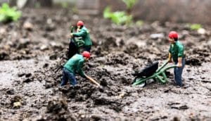 three figurines work in soil with tools and wheelbarrow