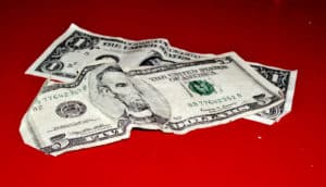 A crumpled one and five dollar bill sit on a red surface.