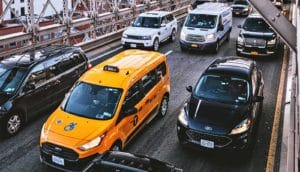 Cars on a bridge in bumper-to-bumper traffic, including a yellow taxi cab.