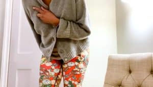 person in sweater and colorful leggings bends with hand to chest
