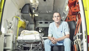 person in scrubs sits in back of ambulance