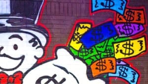 The Monopoly man painted on a brick wall with a money bag with colorful dollar bills flying out.