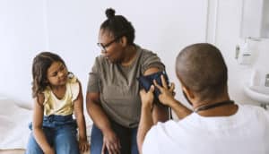 child sits next to adult having blood pressure taken