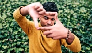 A person holds up their thumbs and forefingers to make a frame around their face.