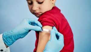 A young boy wearing a red shirt gets a bandaid applied over a vaccination site.