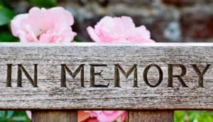 A memorial bench made of wood has the words "In memory" inscribed on it.