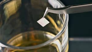 The QR code is on a very small piece of edible silk held over a glass of whiskey with metal tweezers.