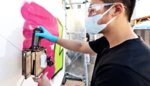 A research loads the robot, which hangs against a white canvas, with a spray paint can.