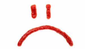 Ketchup on a white background in the shape of a frowning face.