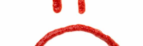 Ketchup on a white background in the shape of a frowning face.