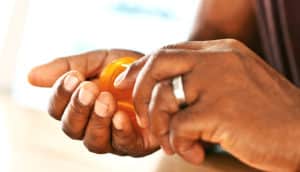 A man pours pills from an orange prescription bottle into his palm.