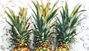 Three pineapples arranged next to each other on white marble to show off their green leaves.