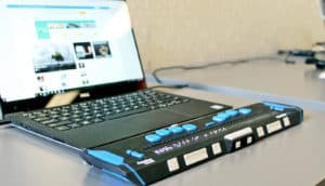 A screen reader attached to a laptop has a refreshable Braille display.