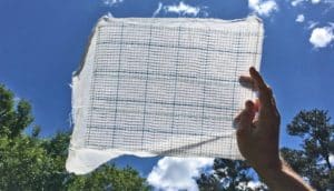 A person holds up a rectangle of the special textile, showing a grid pattern within the fabric.