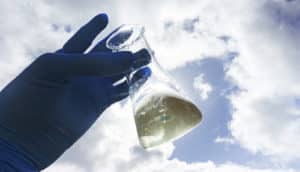 gloved hands holds beaker of water to sky