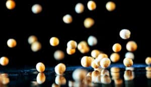 Yellow peas bounce off of a mirrored surface against a black background.