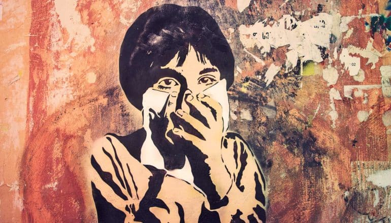 Art on a wall in Tblisi, Georgia shows a young child covering their face with both hands and a handkerchief.