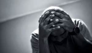 A man holds his hands on his head while looking down.