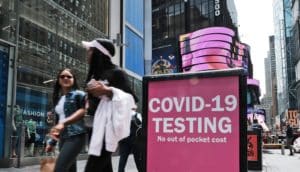 Two people walk past a sign that reads "COVID-19 testing" in Time Square.