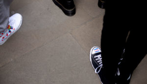 shoes of three people; one has trans flag painted on it