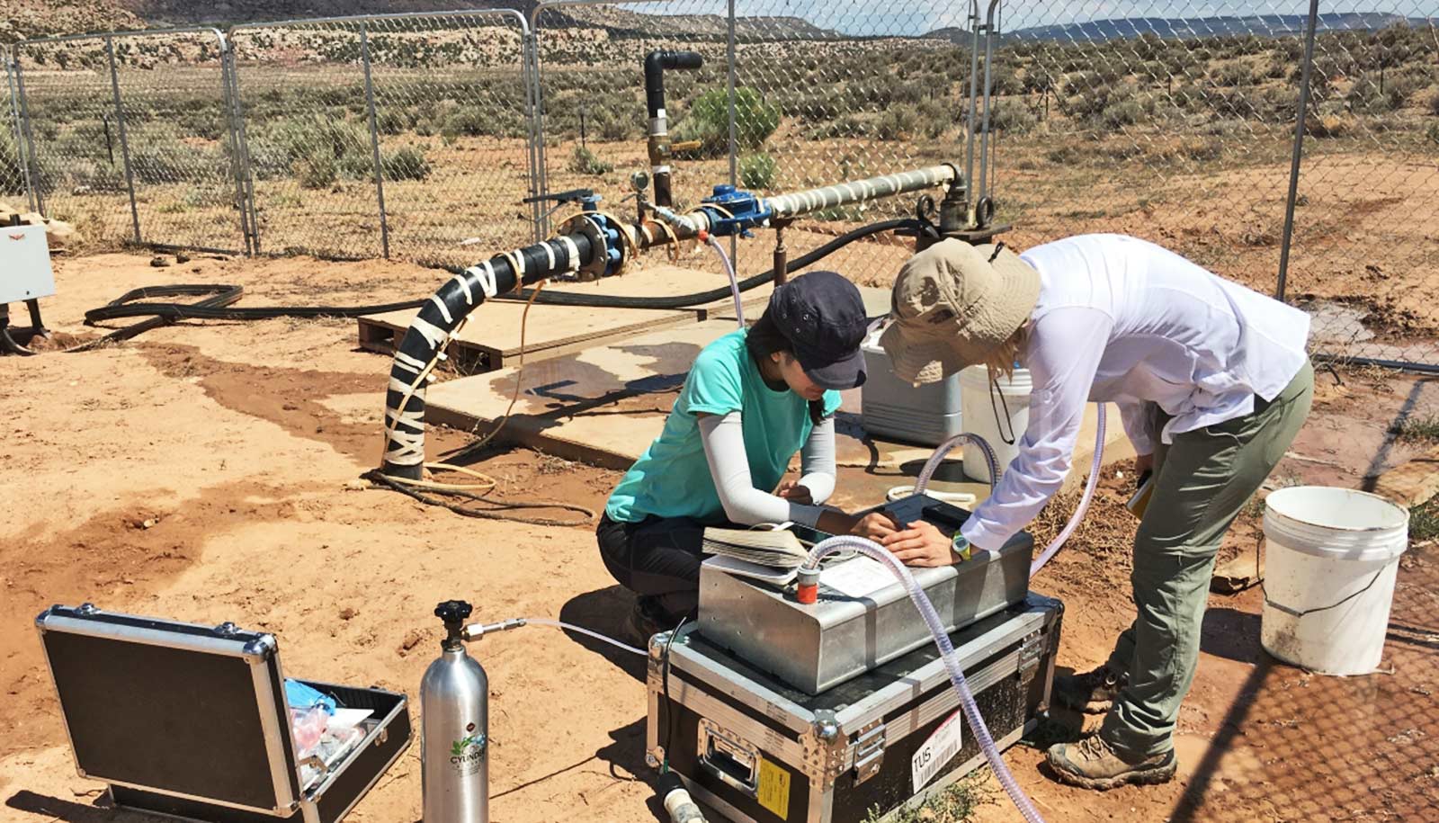 Two researchers lean over equipment with tubes coming out of it in the desert.