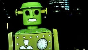 A green toy robot shot up close with a city at night in the background.