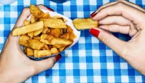 A woman with red nails eats french fries over a blue and white checkered table cloth.