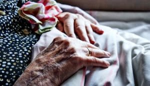 An elderly woman's hands on a blanket in a hospital bed.